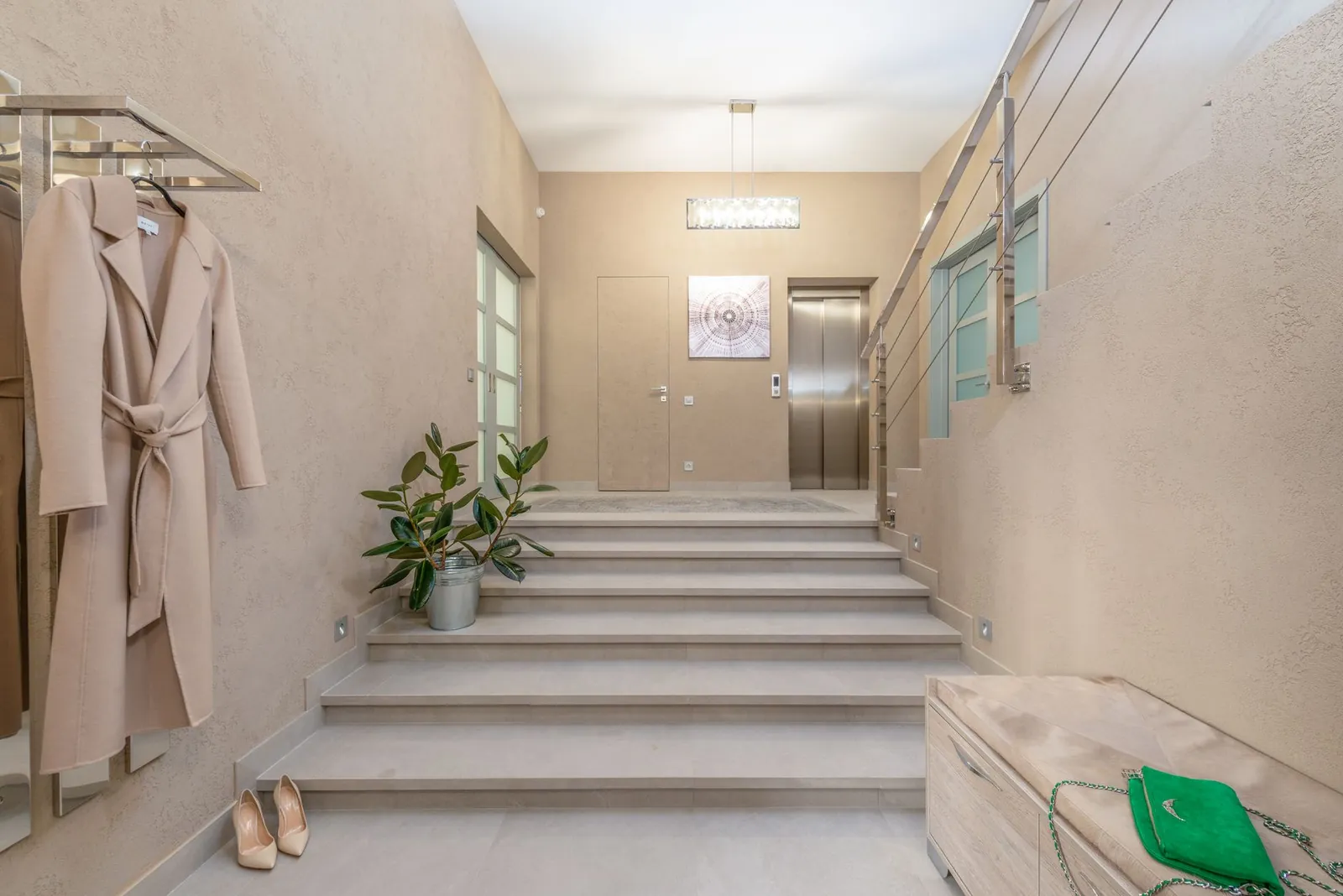 Modern lobby with elevator and wide staircase leading to hallway with bench and hanger shelf