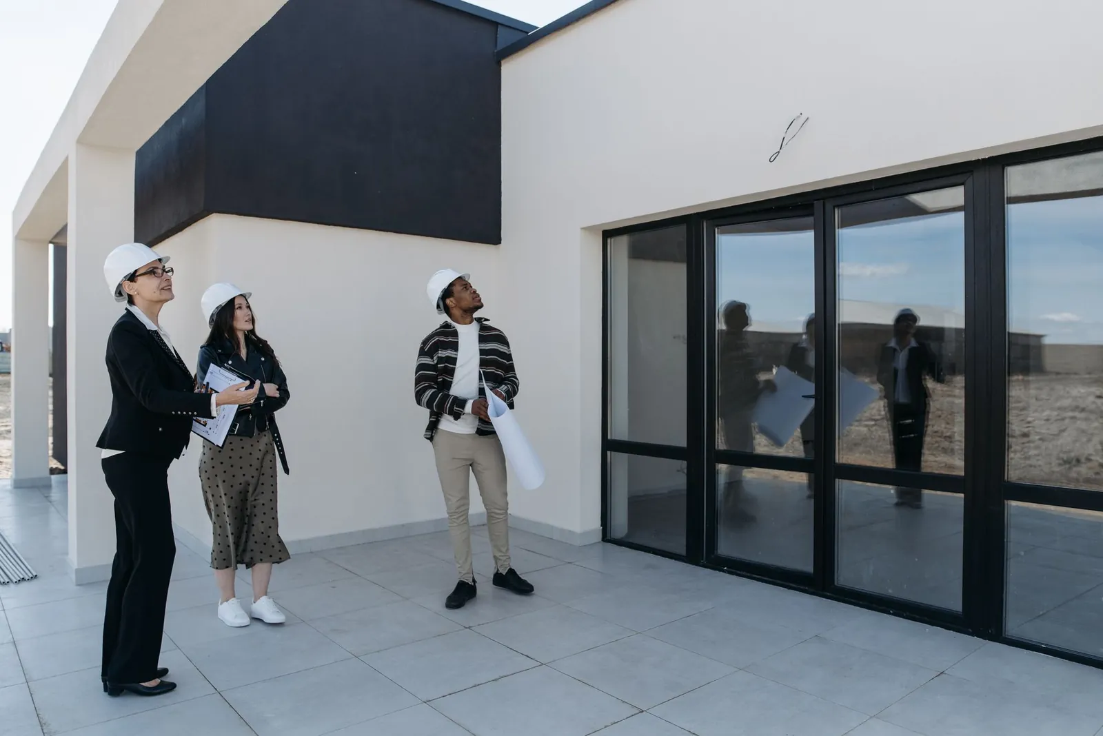 Three people in hard hats inspecting the exterior of a newly built building