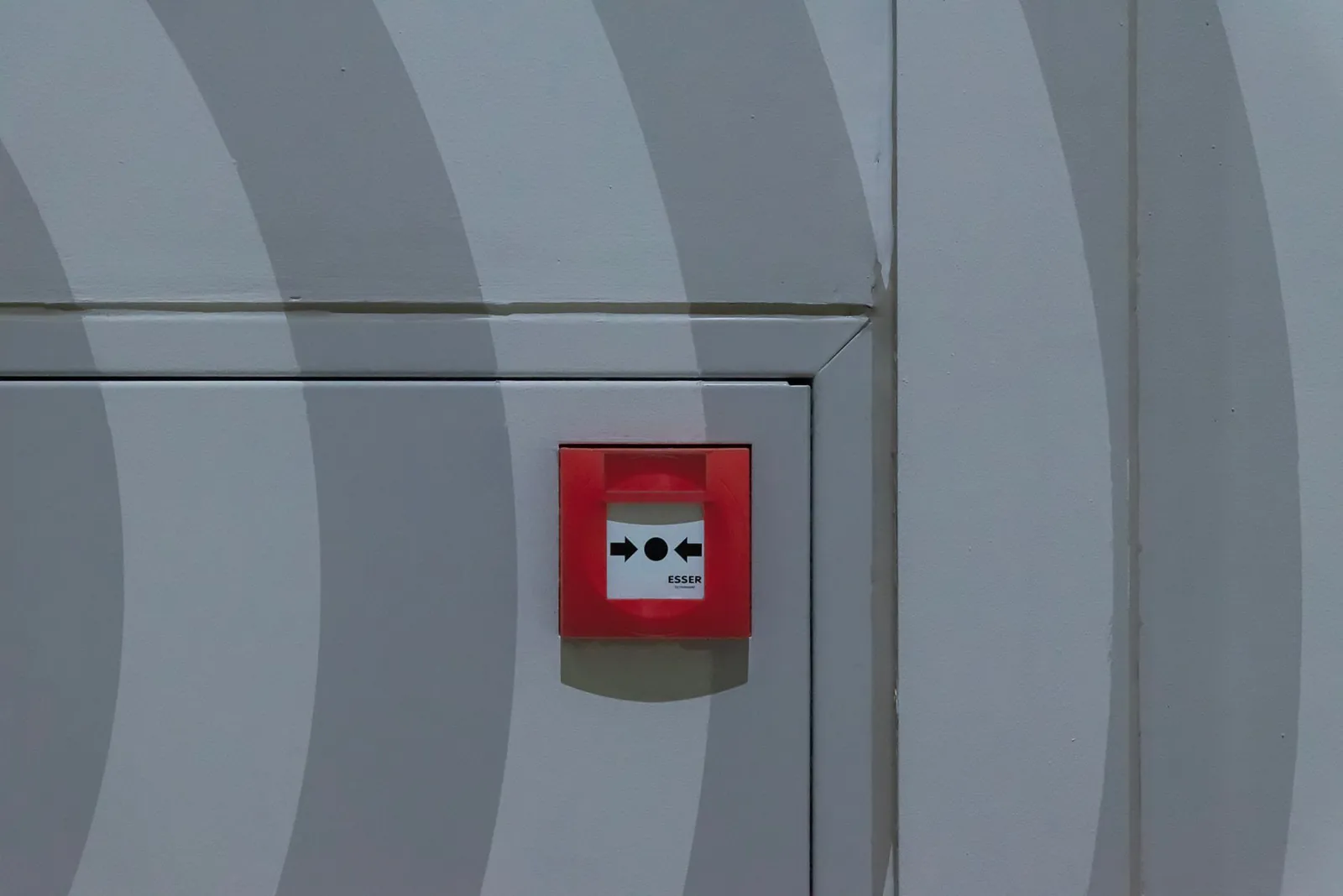Red emergency button on a grey patterned wall, emphasizing safety measures.