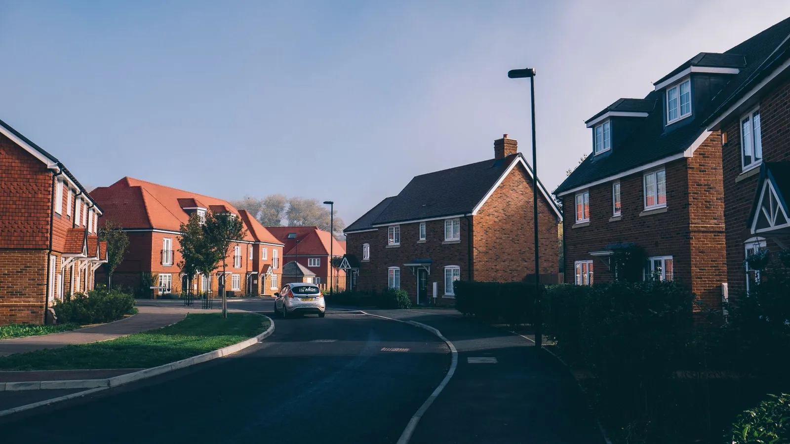 New-build red-brick houses along a curving estate road with a grass verge