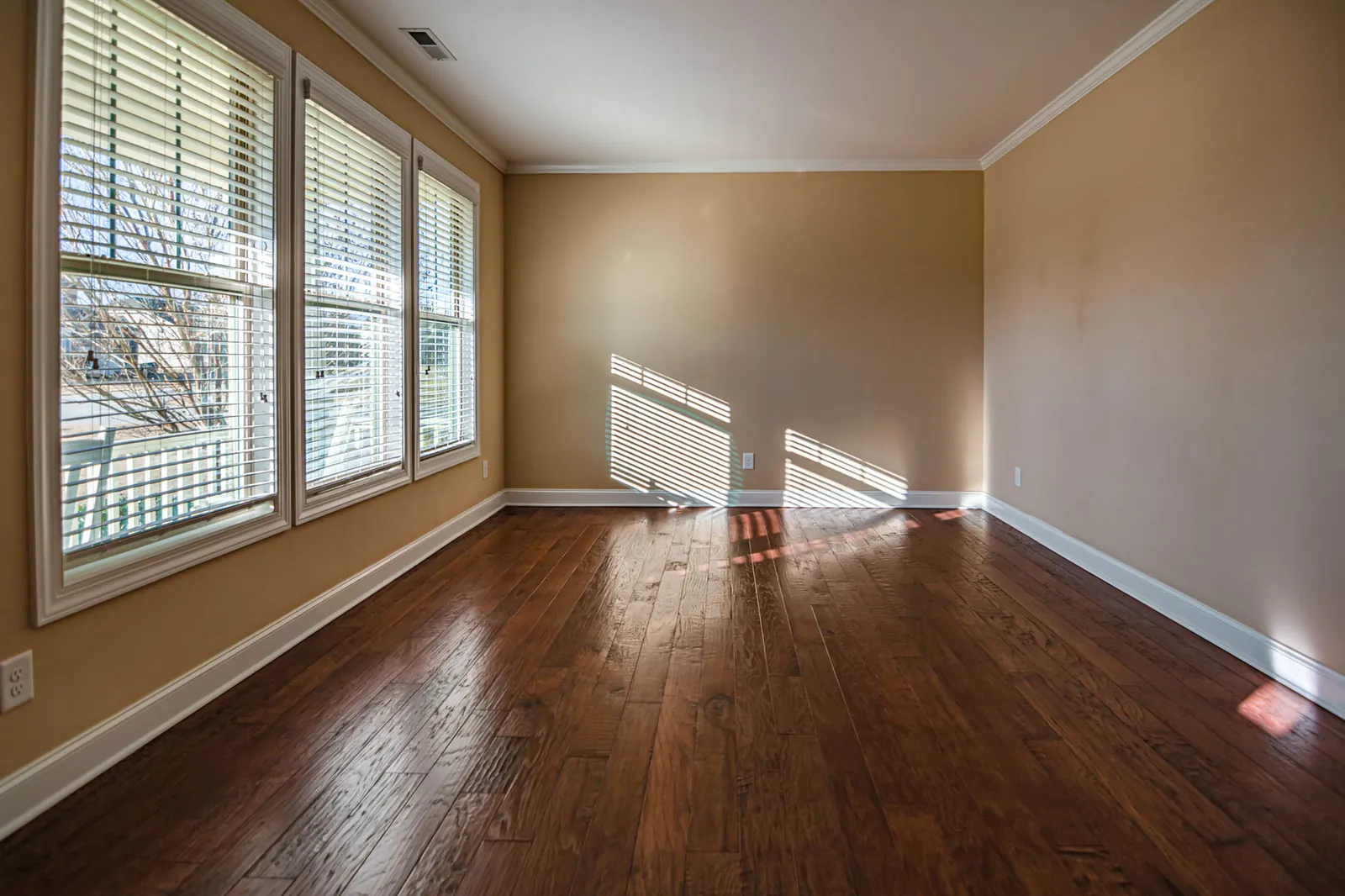 Empty sunlit room with wooden floorboards and blinds at the windows