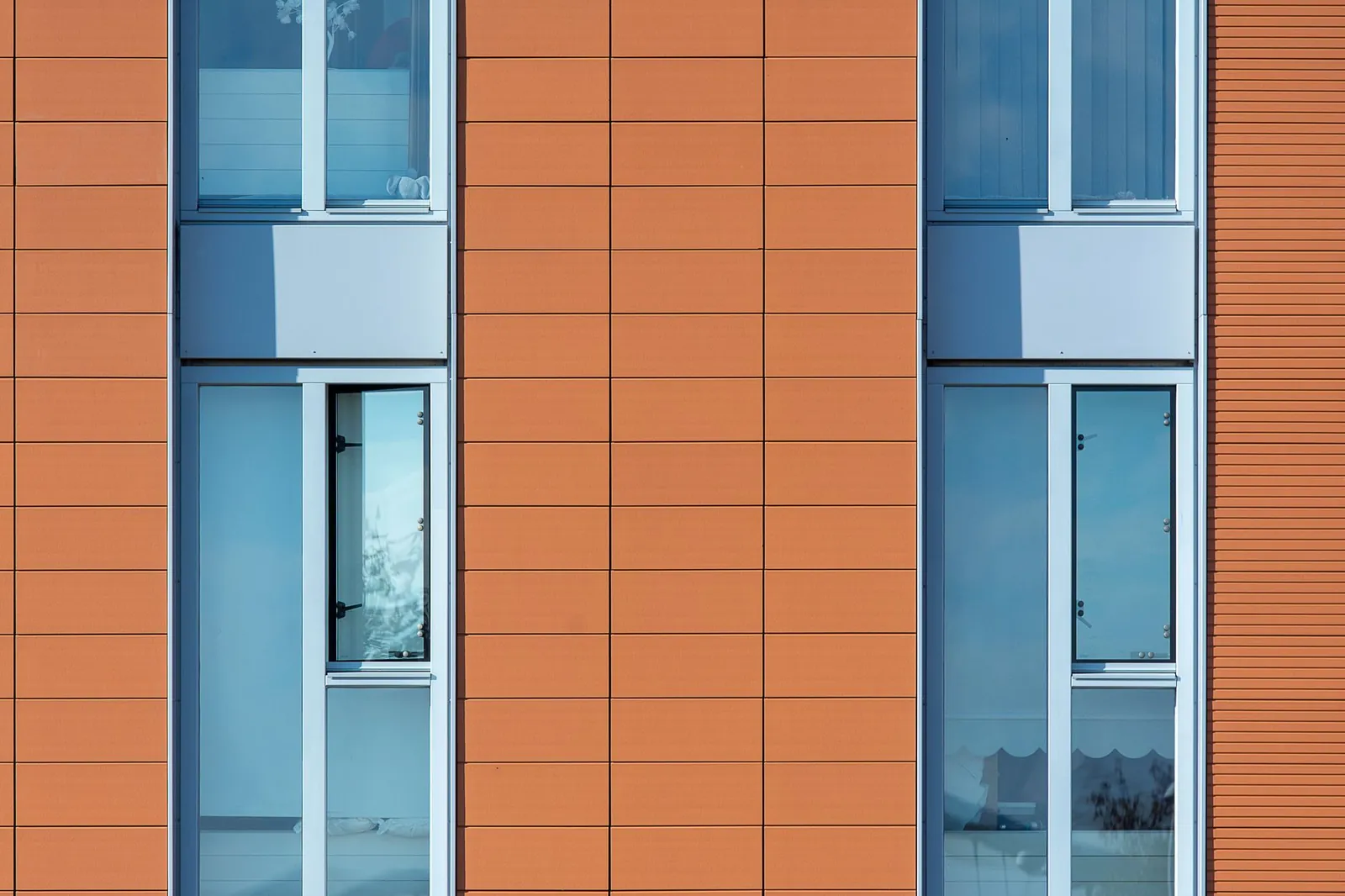 Close-up of an external wall with terracotta-coloured cladding panels and windows
