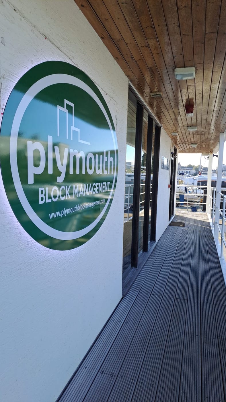 The Plymouth Block Management sign on the office walkway, with boats in the marina beyond